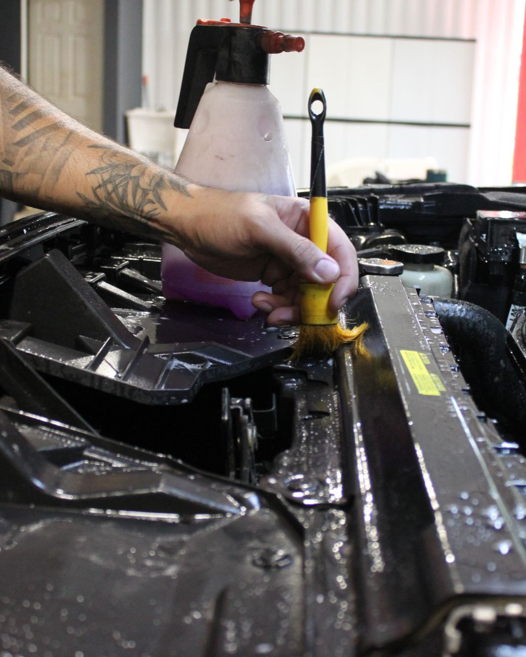 A person standing on a step ladder washes a white Toyota Tacoma truck inside a well-lit bay.