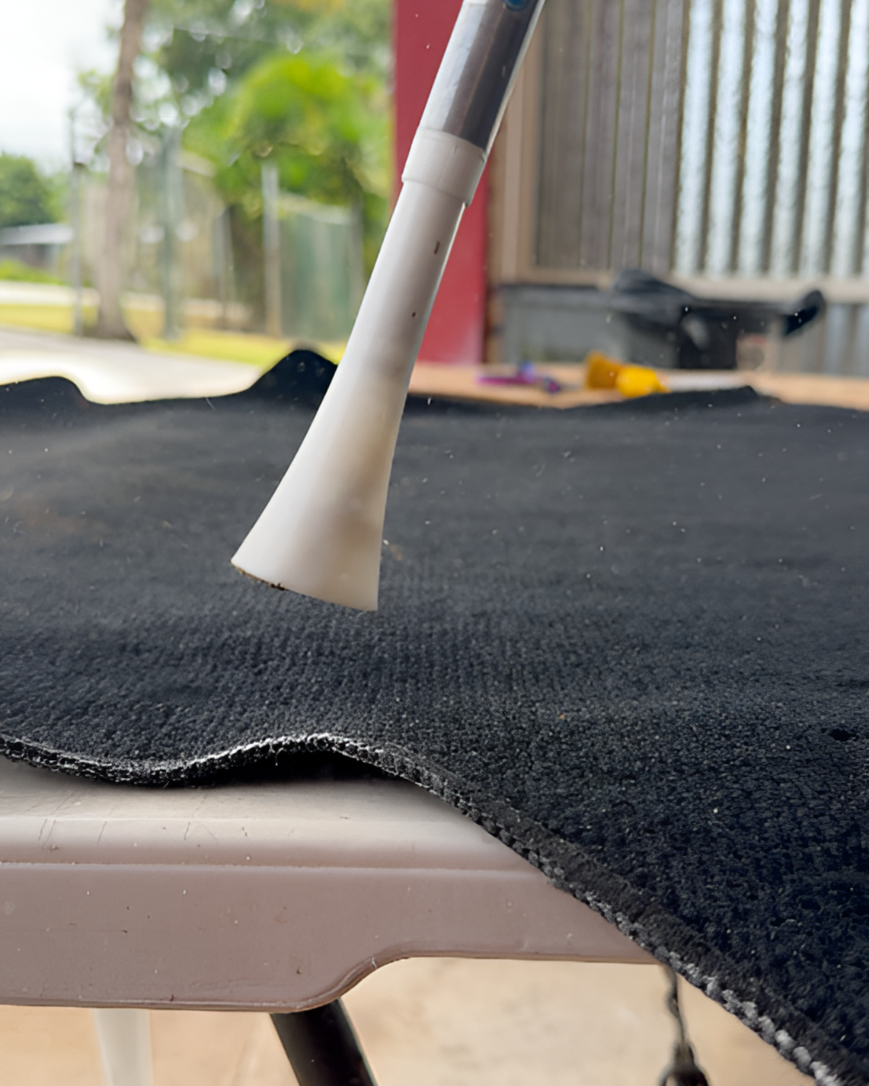 A handheld white vacuum attachment hovers just above a piece of black fabric resting on a white table.