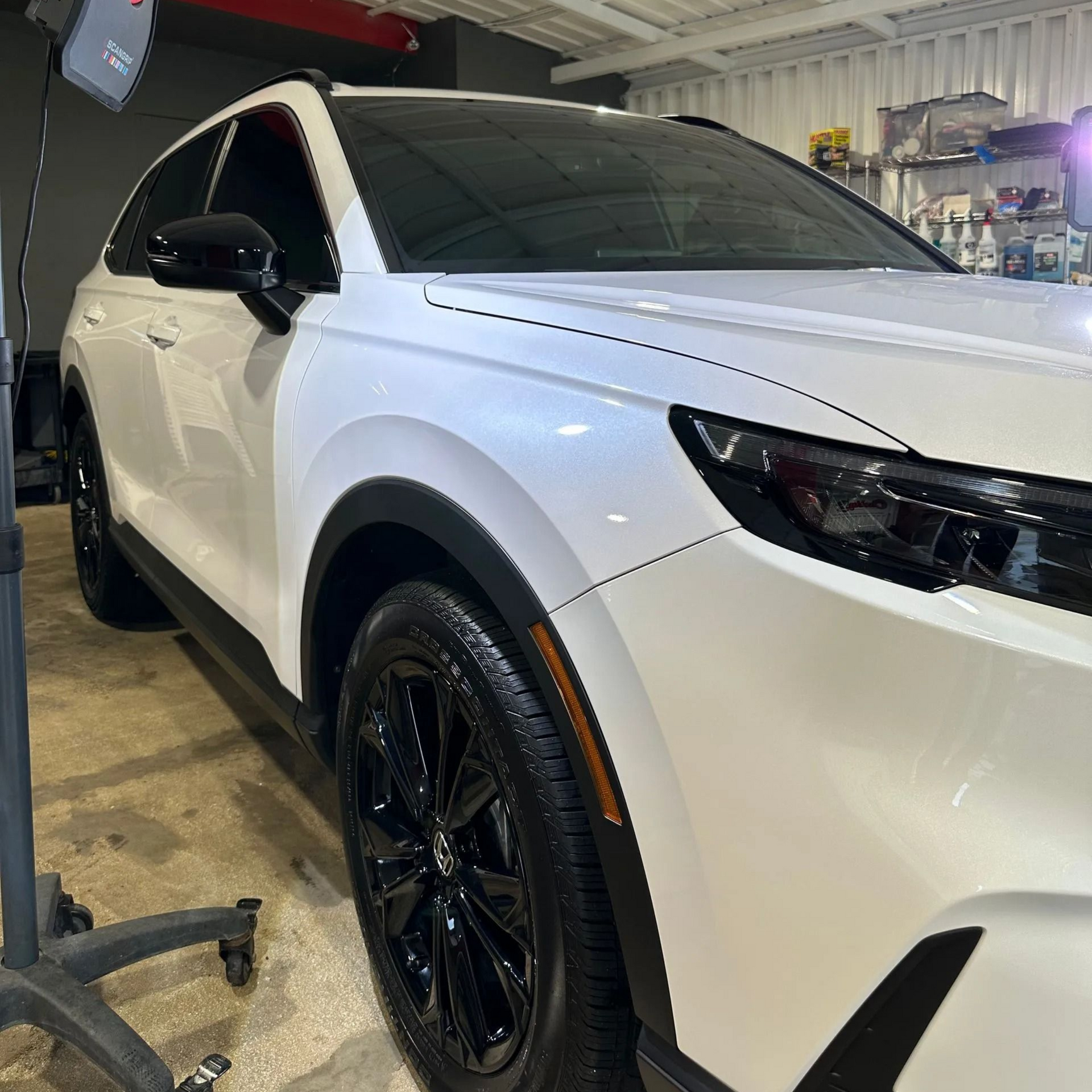 A white SUV with black rims and trim parked inside a garage, angled to show its front passenger side.