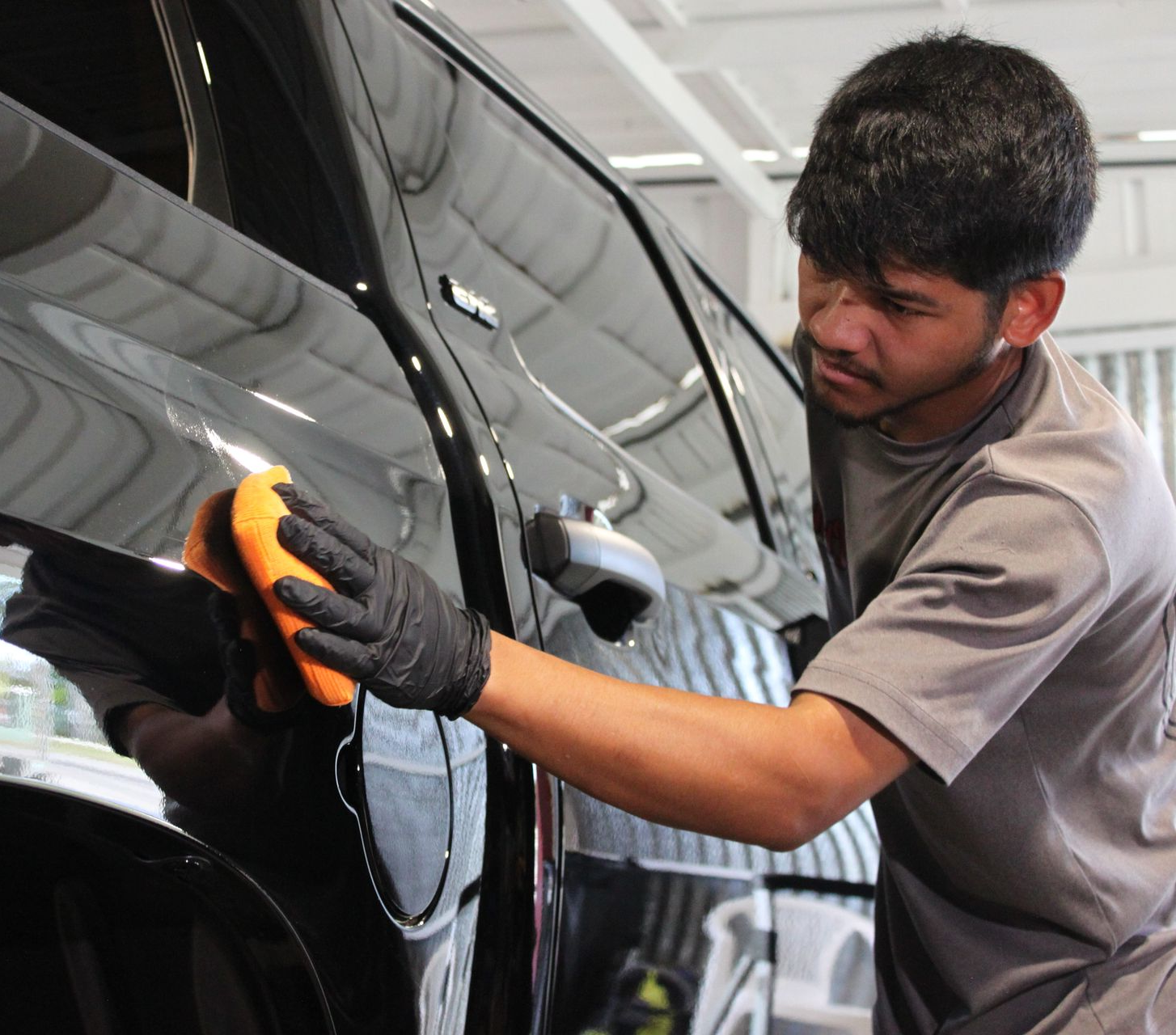 A person wearing black gloves uses an orange sponge to apply product to the black door panel of a Toyota Tundra truck.