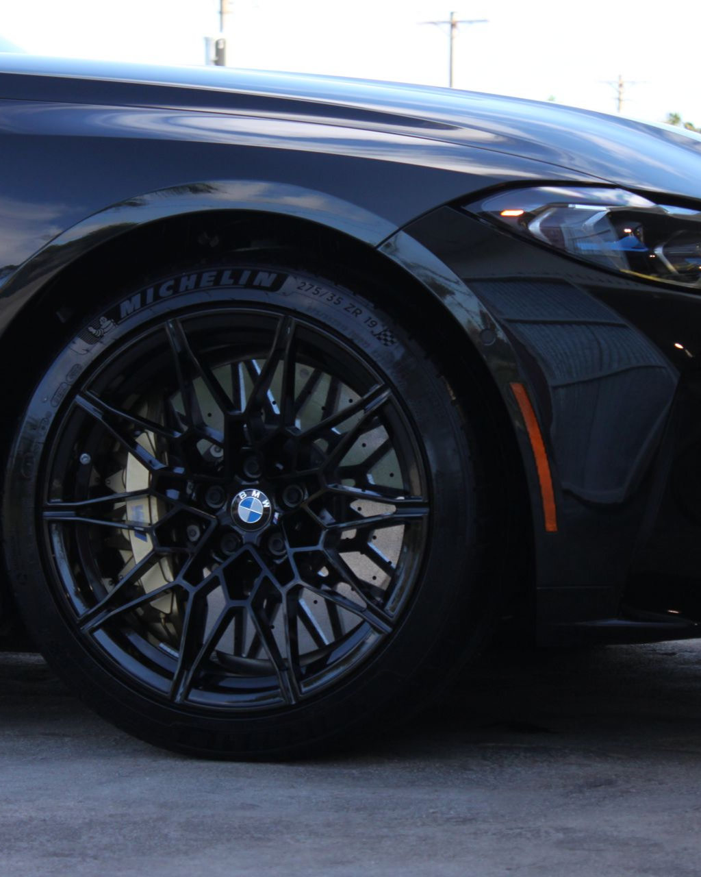 Close-up of a black BMW car's front tire and alloy wheel, featuring a Michelin tire and a dark, multi-spoke rim design.