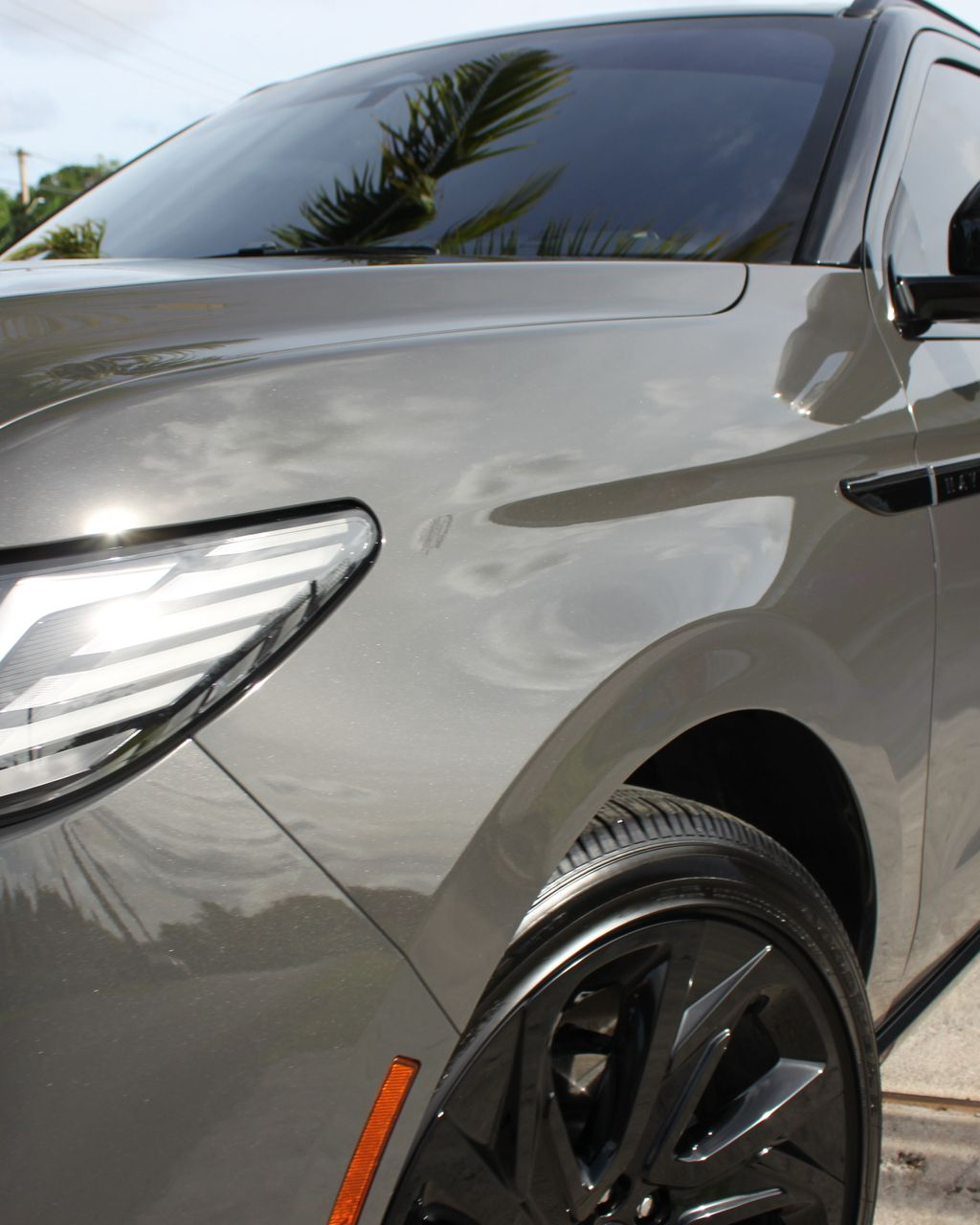 Close-up of the front fender, headlight, and black wheel of a glossy gray SUV outdoors.