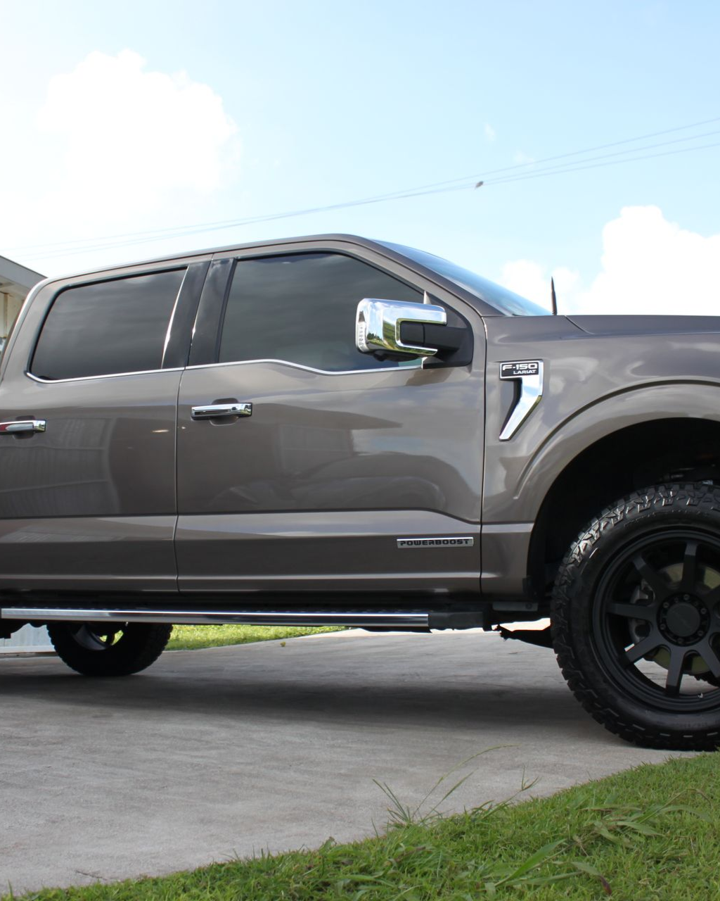 A side view of a gray Ford F-150 truck with tinted windows, chrome trim, and black off-road wheels parked on concrete.