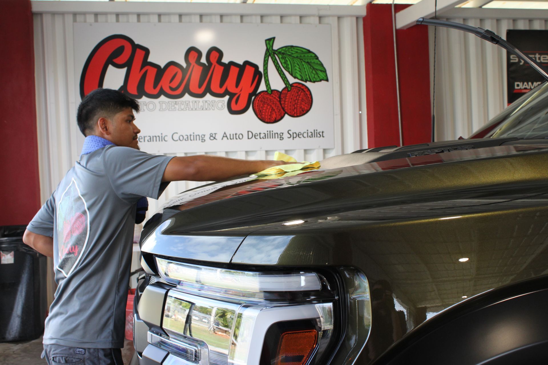 A person standing on a step ladder washes a white Toyota Tacoma truck inside a well-lit bay.