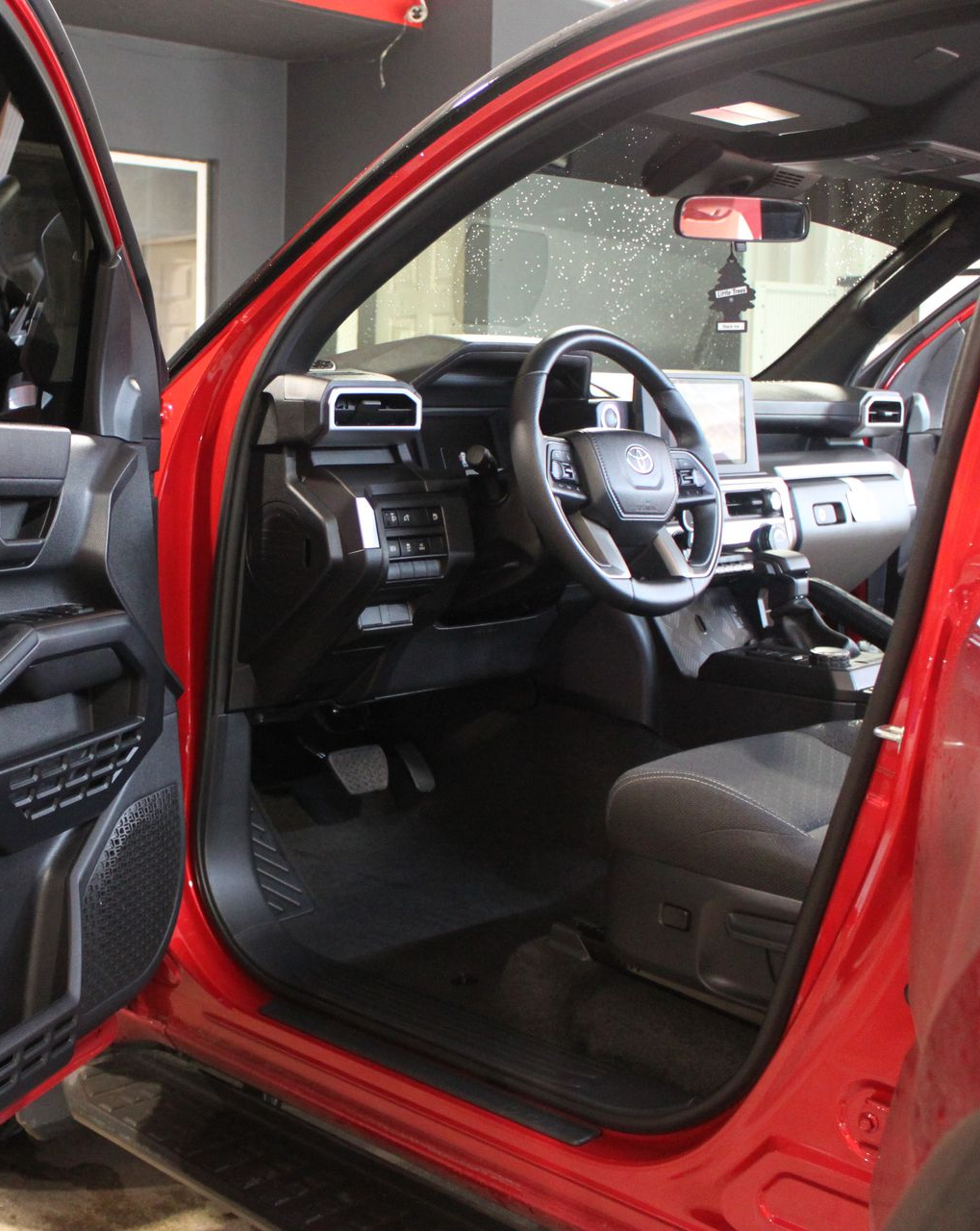 The open driver-side door of a bright red vehicle, revealing a dark interior, steering wheel, and dashboard.