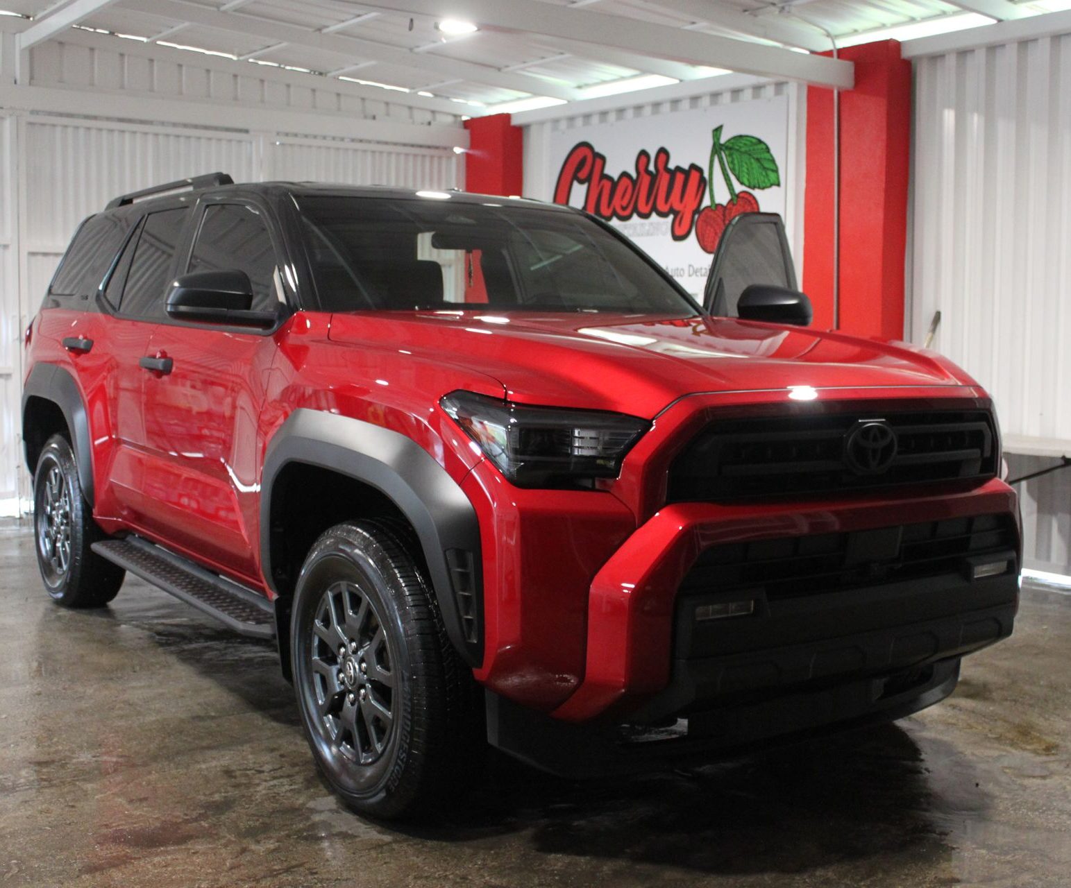 A person standing on a step ladder washes a white Toyota Tacoma truck inside a well-lit bay.