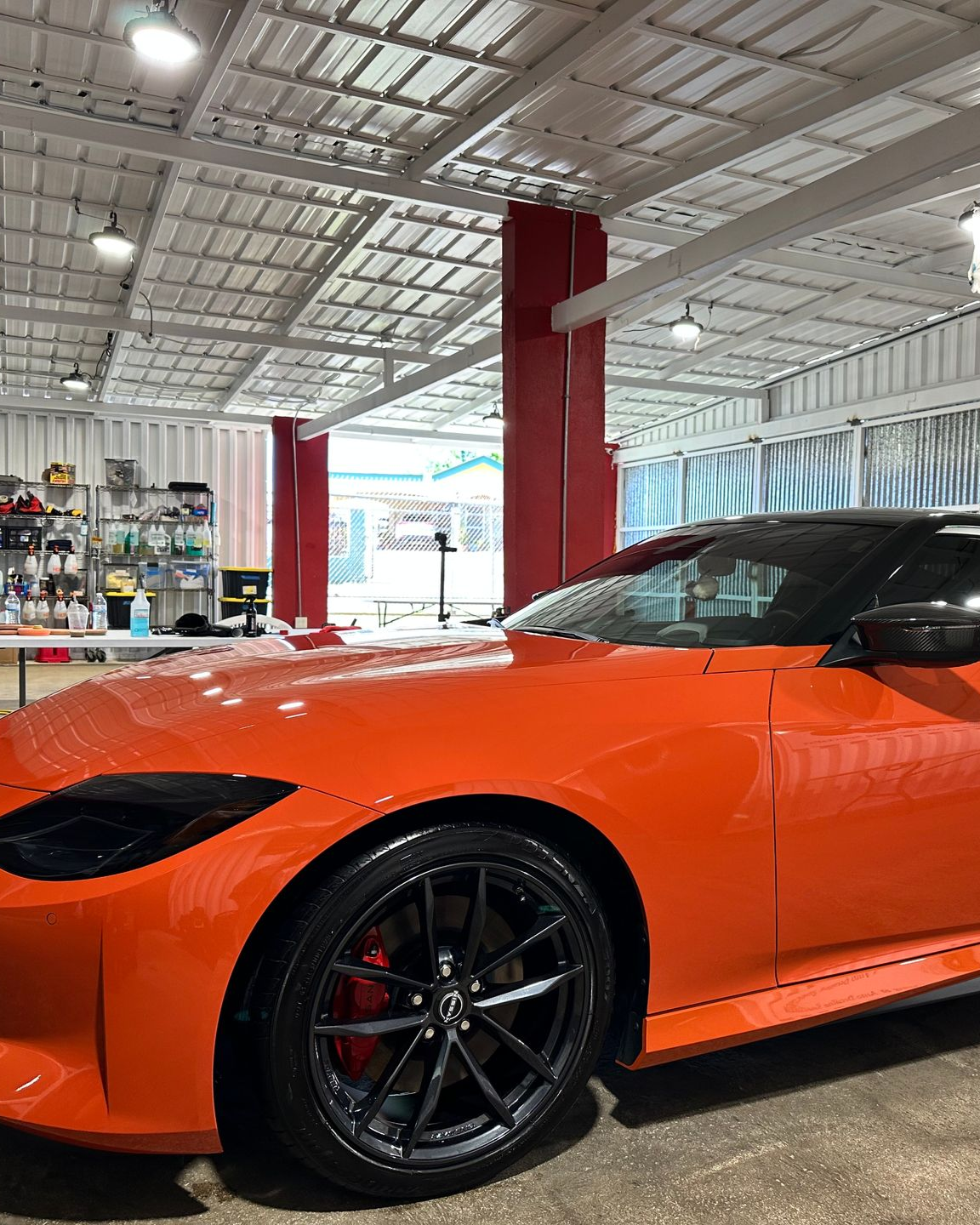 A bright orange Nissan Z sports car parked inside a brightly lit industrial garage.