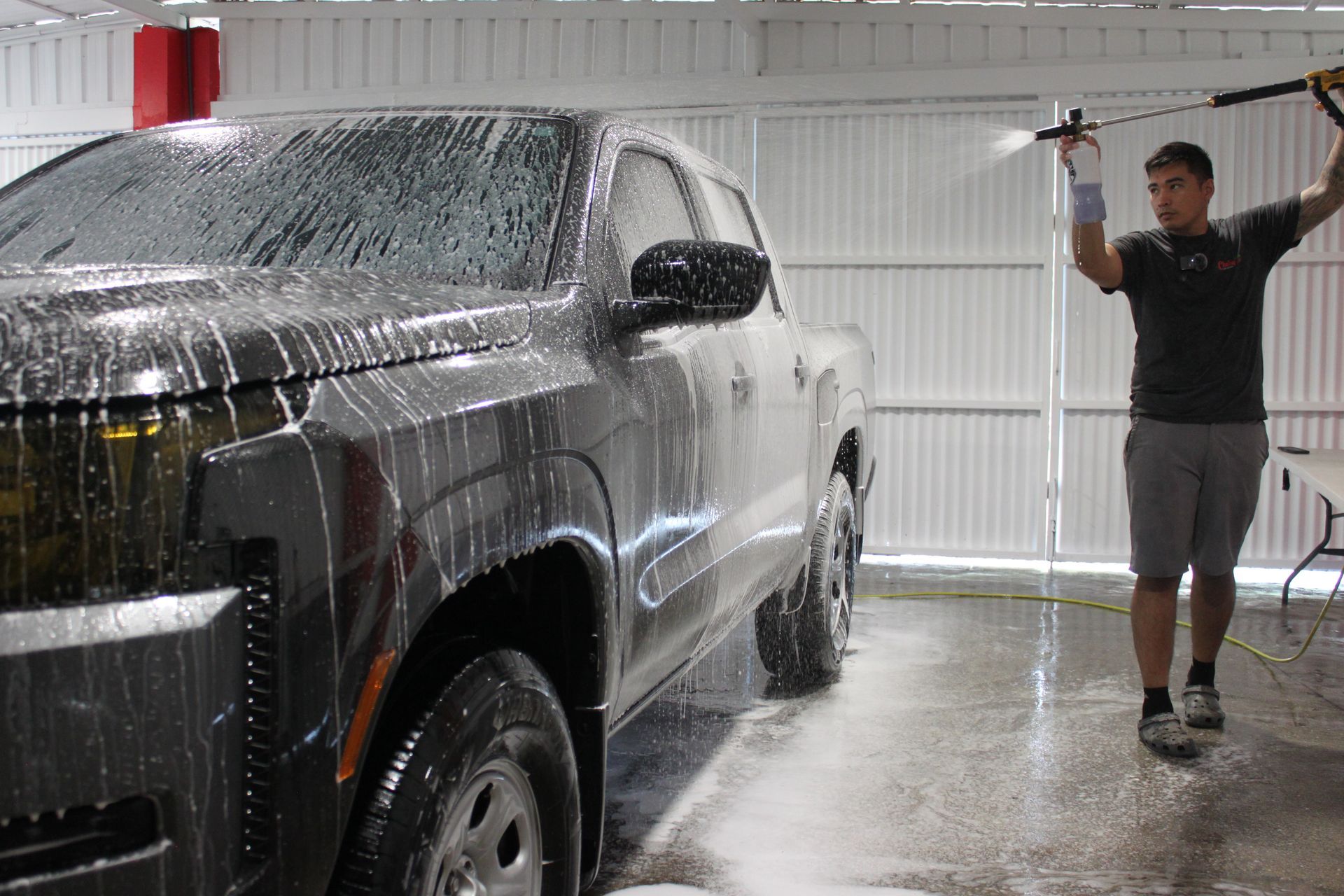 A person sprays soap foam onto a dark pickup truck inside a garage.