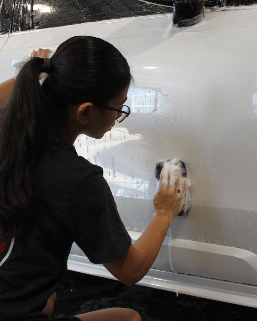A person washing a white car using a soapy sponge.