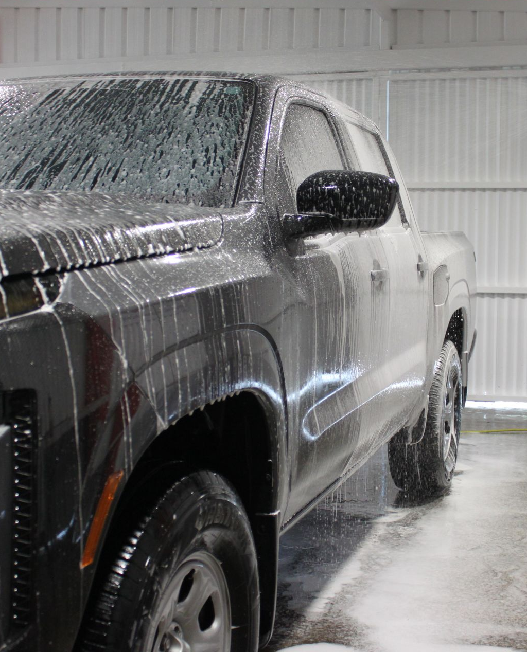 A silver car is being washed with soap and water