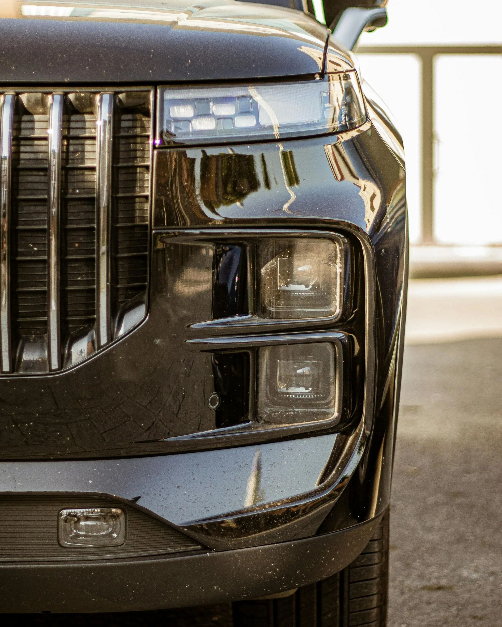 Close-up of a modern, black SUV front end featuring a chrome vertical grille, stacked headlights, and LED lighting.