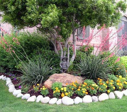 White vinyl fence with landscaping: bushes, mulch, and green lawn.