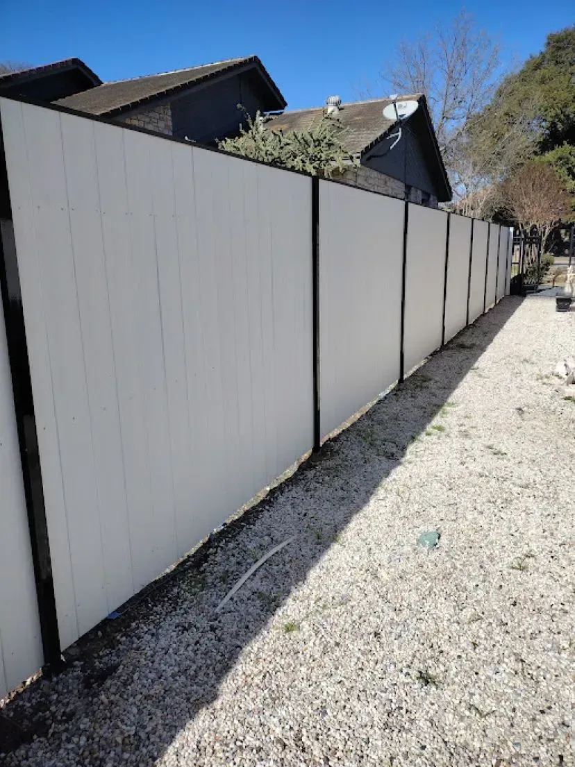 White and black fence, outdoor setting, gravel ground, houses in background.