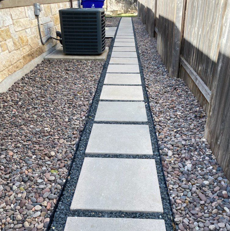 Stone pathway between fences and gravel, near an air conditioning unit.
