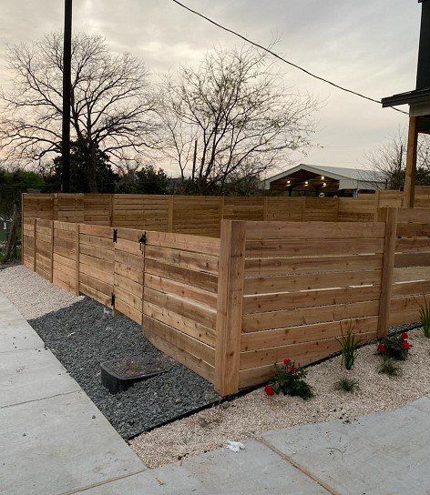 Wooden fence with gravel and small plants beside a sidewalk.