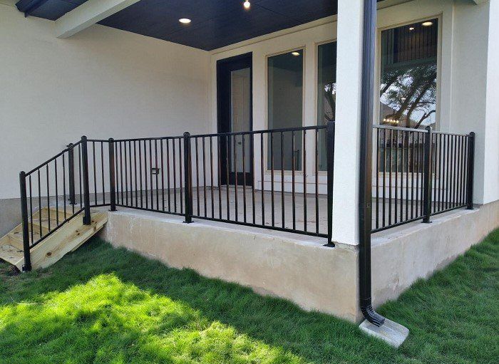Black metal railing encloses a patio with a step, overlooking a lawn.