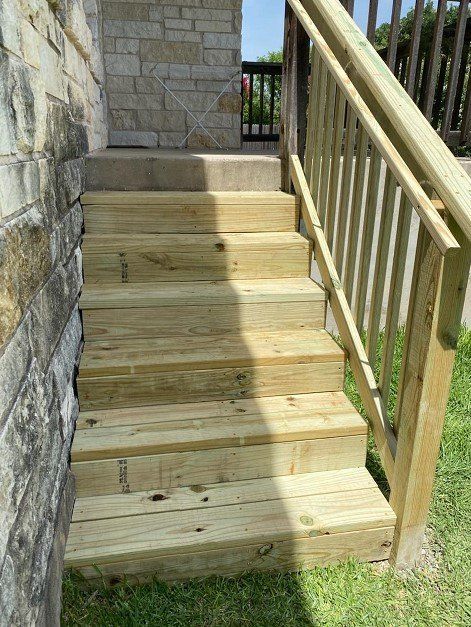 Wooden outdoor staircase with a railing, leading up to a stone wall entrance.