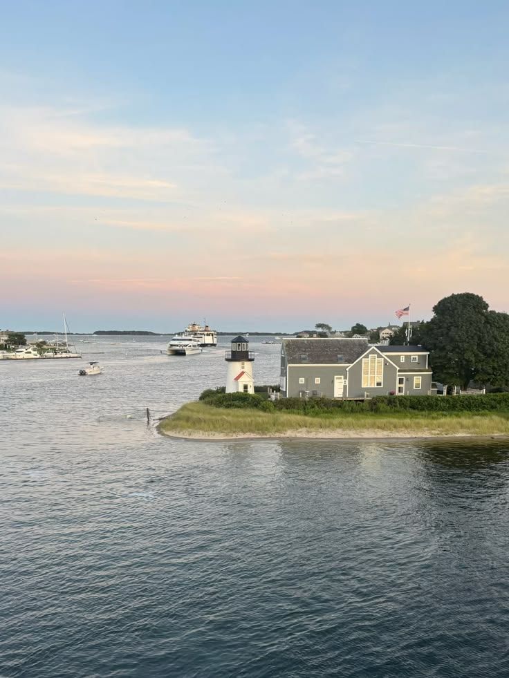 Coastal harbor at sunset with calm water, boats, and gray houses on a small shoreline point