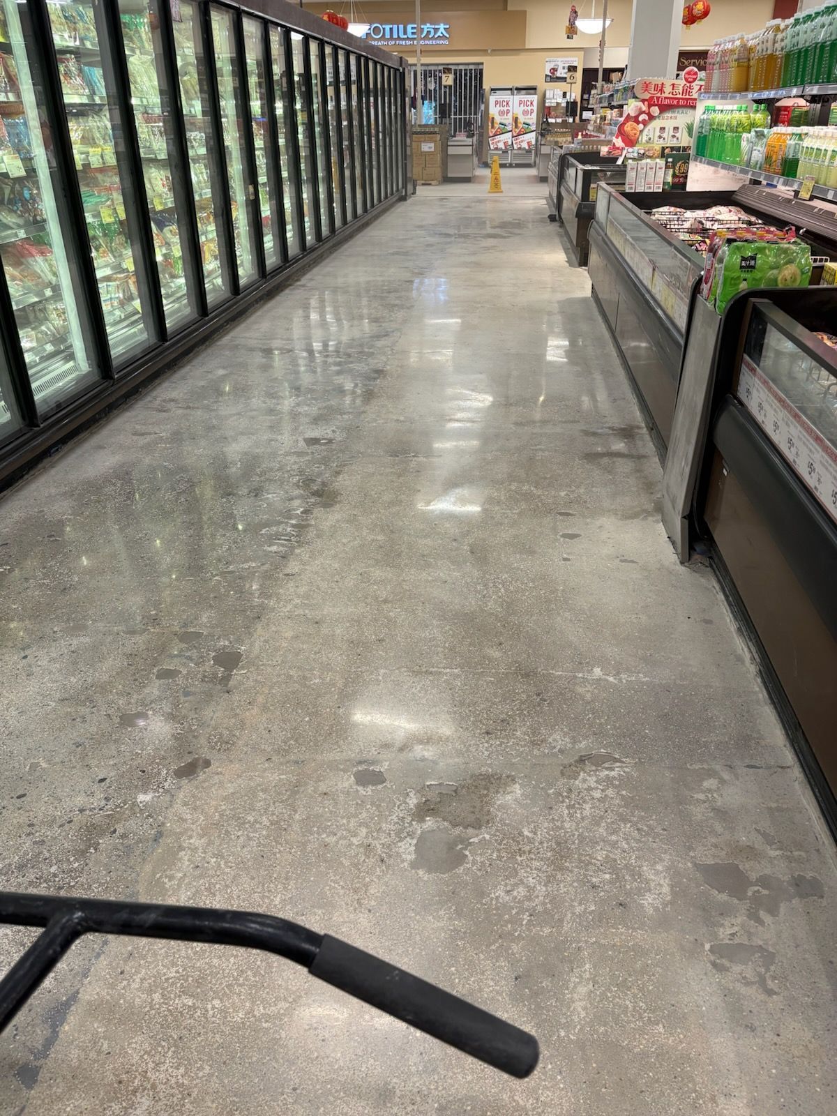 polished concrete in a Grocery store aisle with freezer cases on the left and produce displays on the right, viewed from a shopping cart.