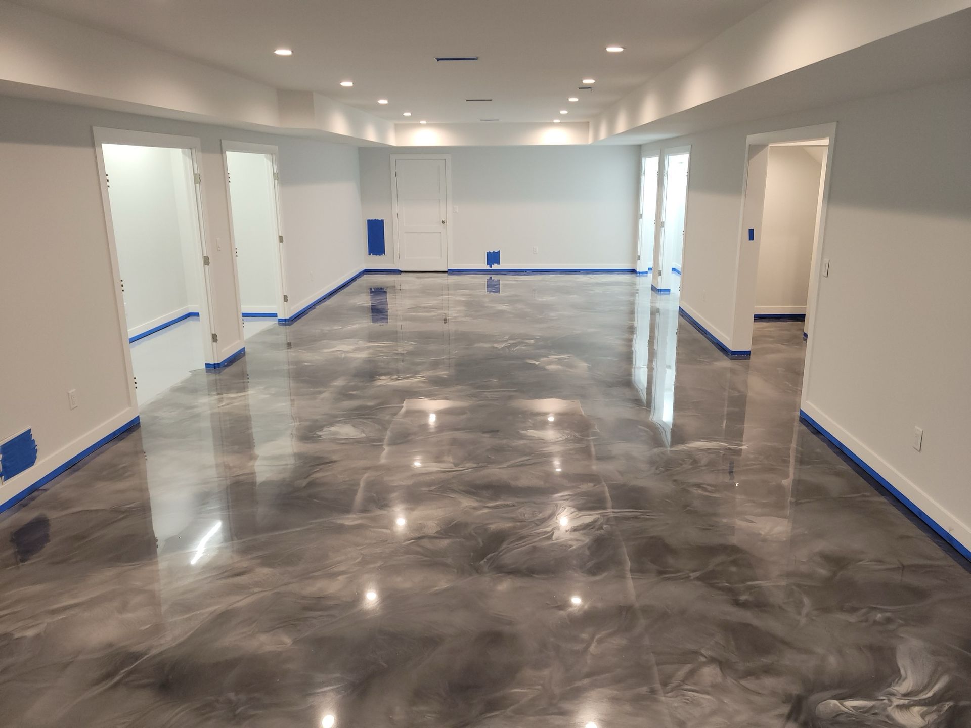 Empty bright room with glossy gray floor, white walls, and blue painter’s tape along the baseboards.