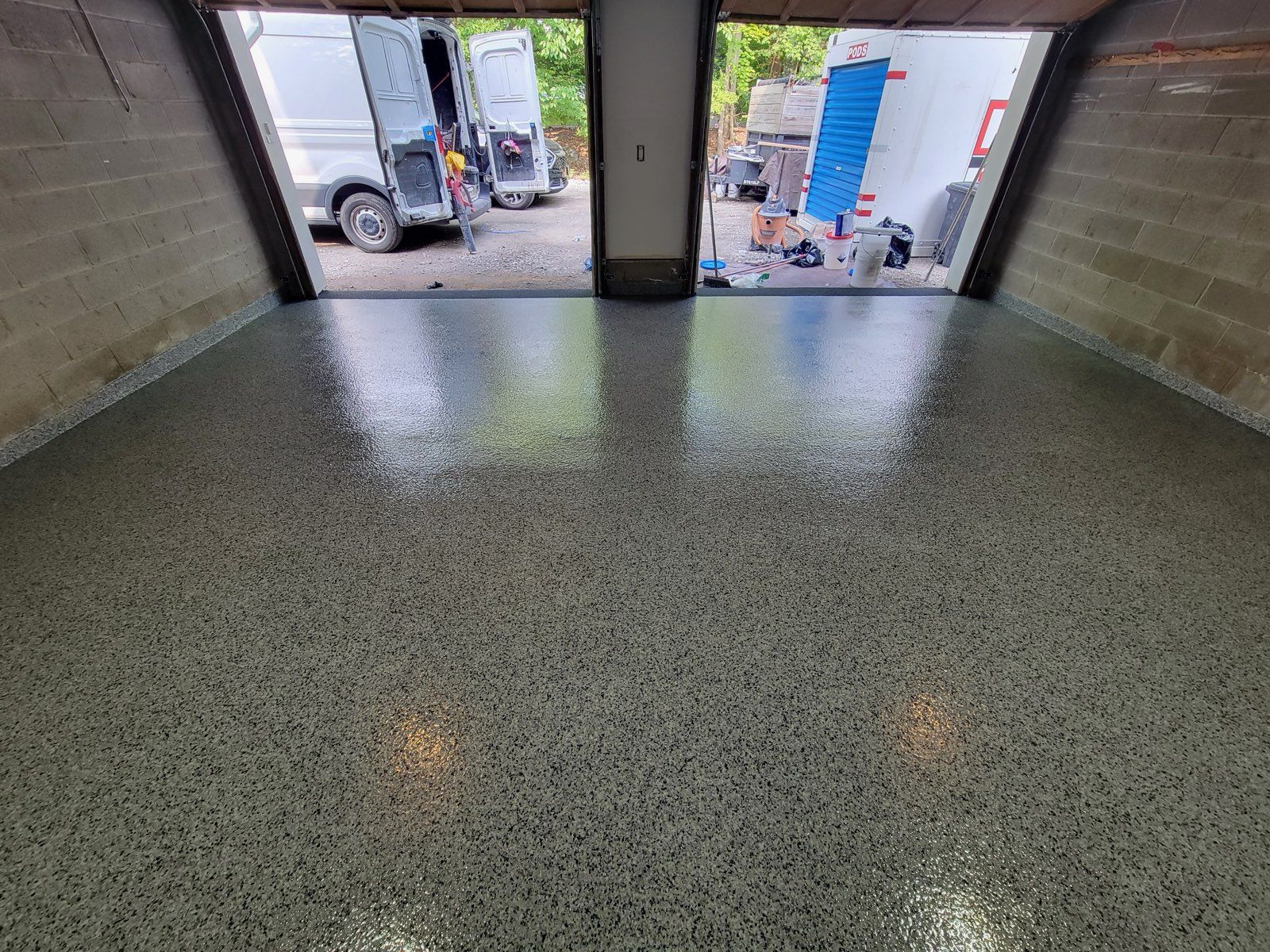 Empty indoor garage opening onto a wet lot with trucks and blue equipment outside