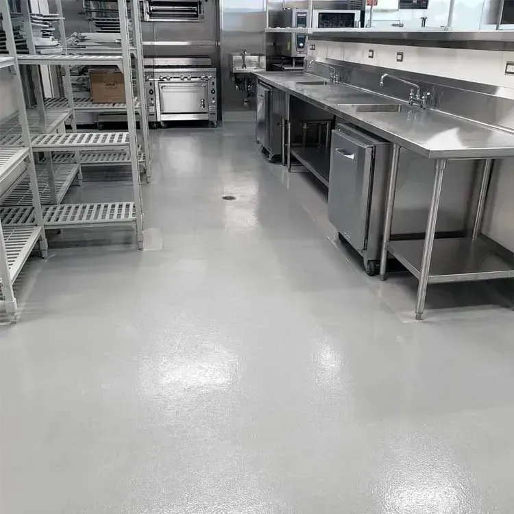 Empty commercial kitchen with stainless steel counters, shelves, and a clean gray floor