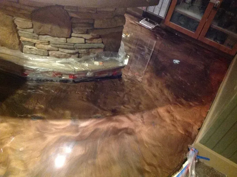Floodwater covering a wooden floor around a stone fireplace and doorway inside a home