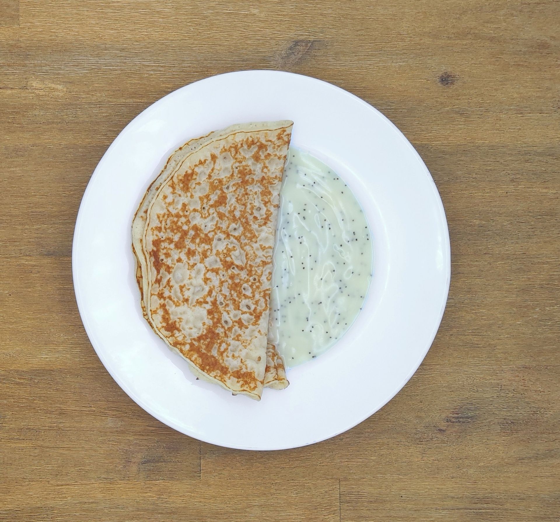 Auf einem weißen Teller mit Apfelmus lagen Crêpes auf einem Holztisch.