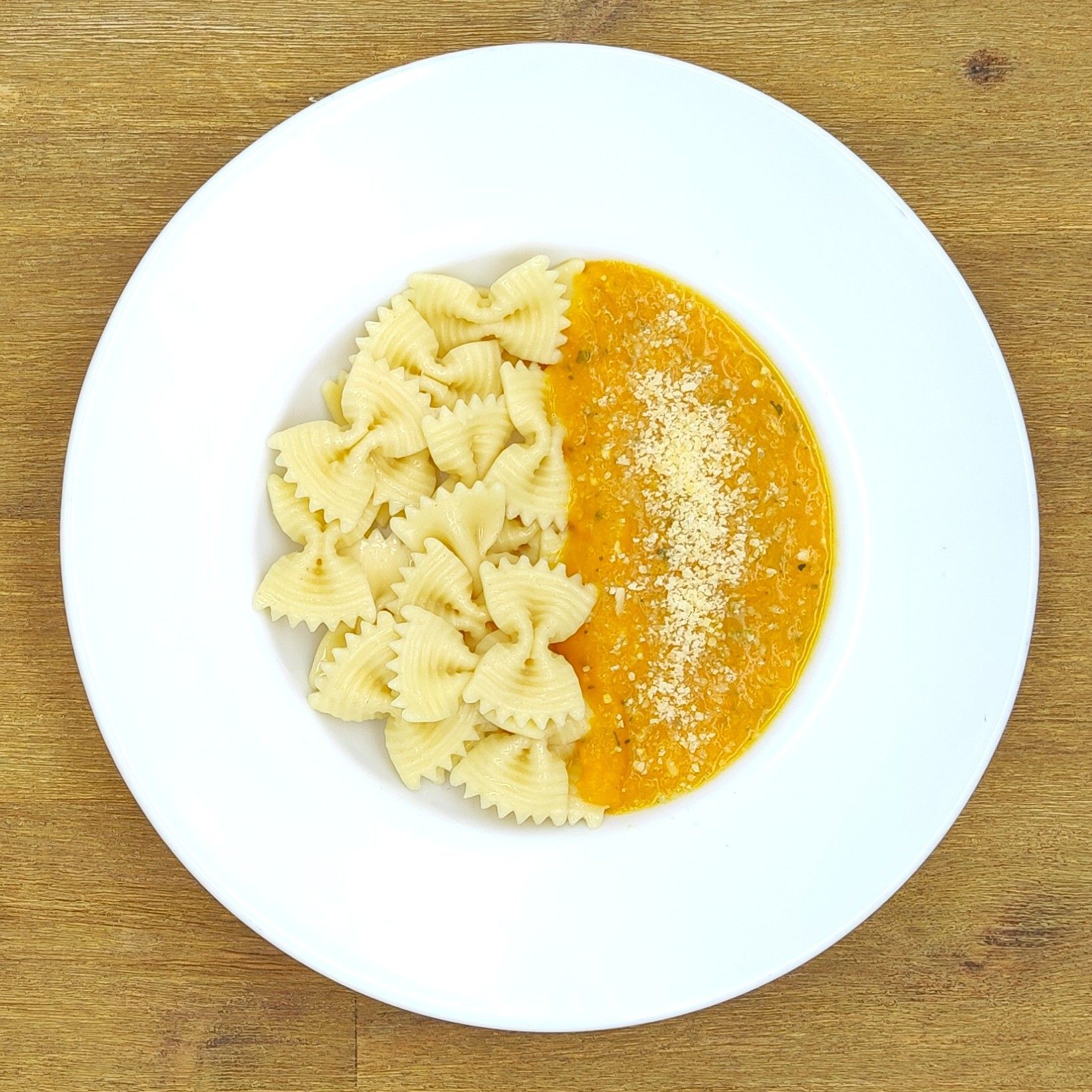 Weißer Teller mit Farfalle-Nudeln und Orangensauce, bestreut mit geriebenem Käse.