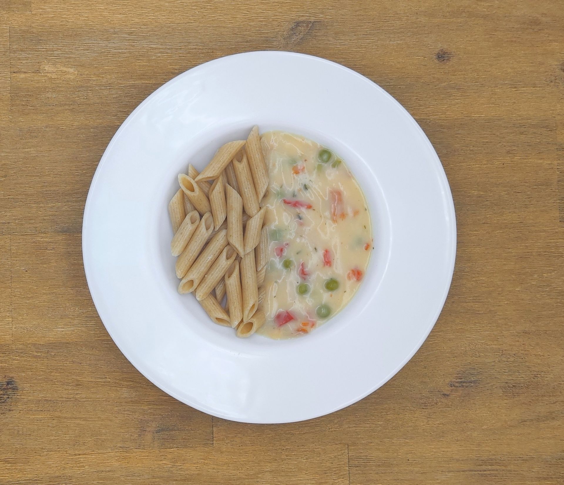 Weiße Schüssel mit Linsensuppe und Brot auf einer Holzoberfläche.