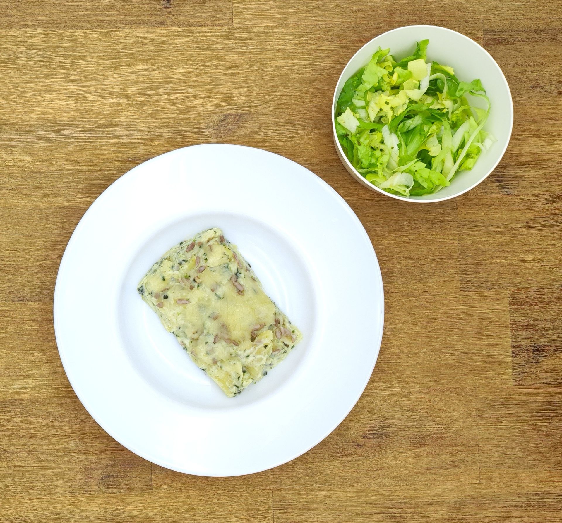 Weiße Schüssel mit Linsensuppe und Brot auf einer Holzoberfläche.