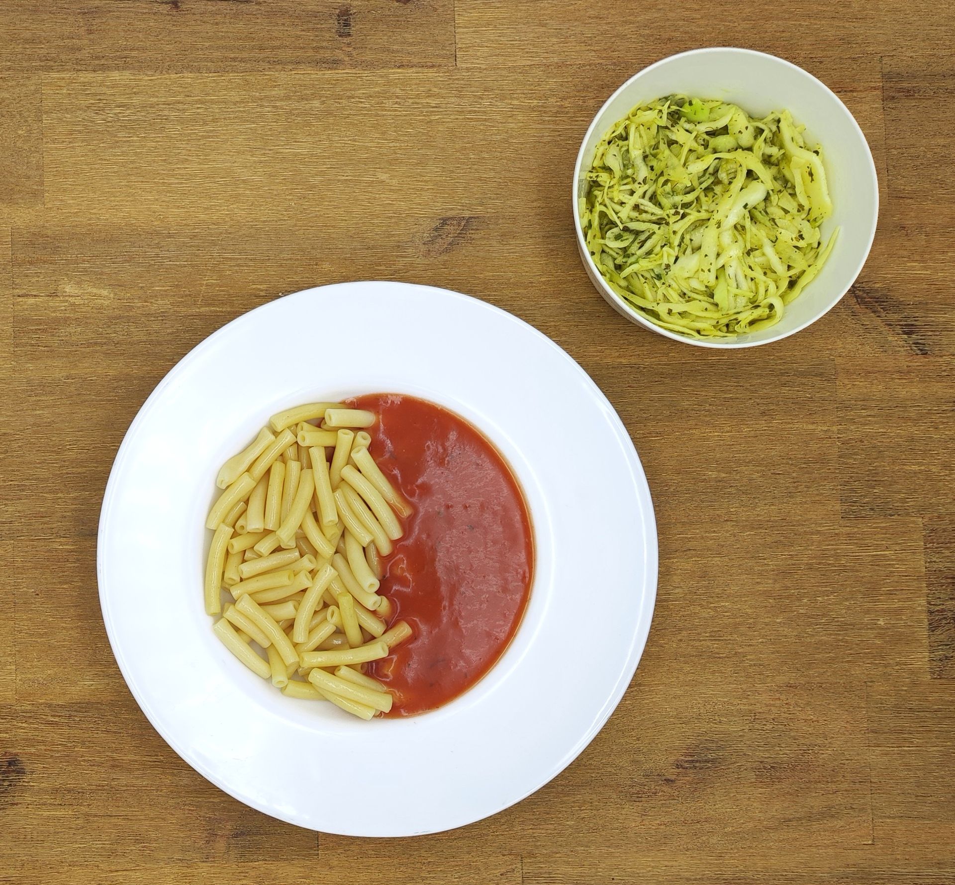 Weißer Teller mit Farfalle-Nudeln und Orangensauce, bestreut mit geriebenem Käse.