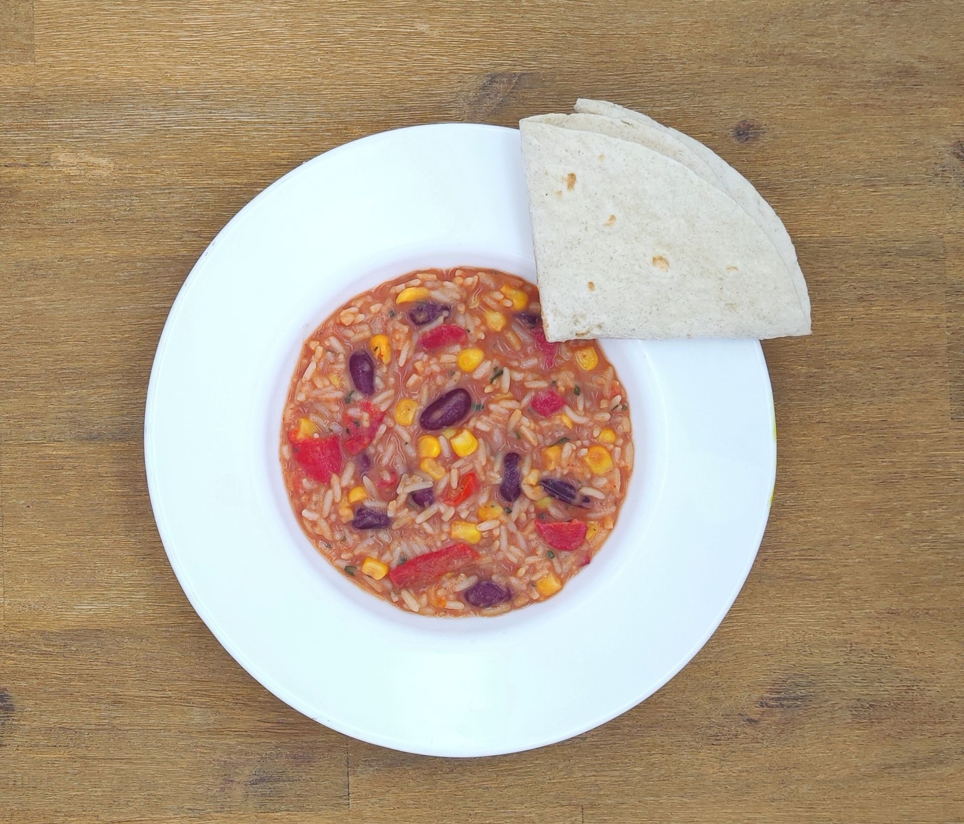 Weiße Schüssel mit Linsensuppe und Brot auf einer Holzoberfläche.