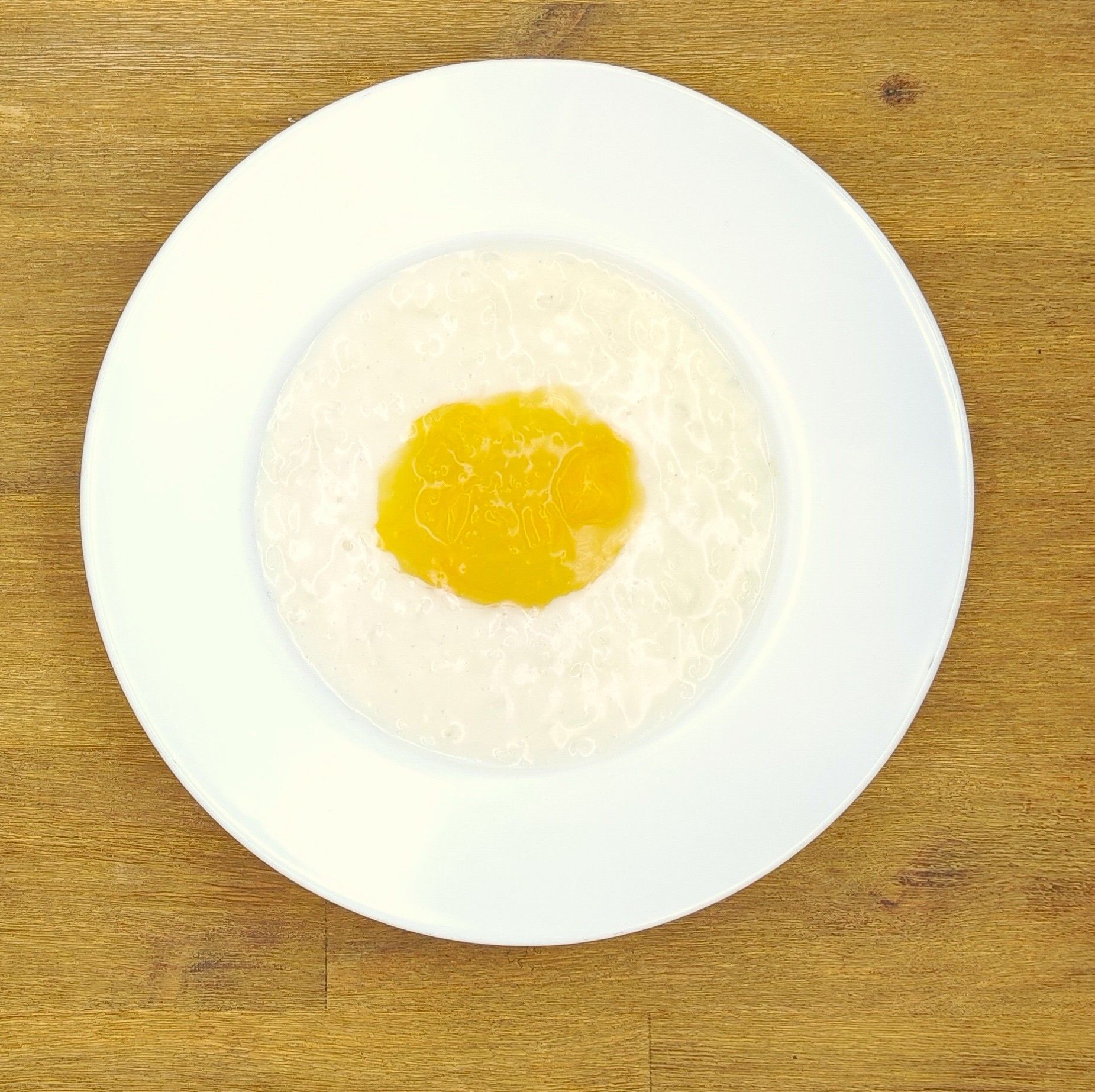 Weiße Schüssel mit Linsensuppe und Brot auf einer Holzoberfläche.