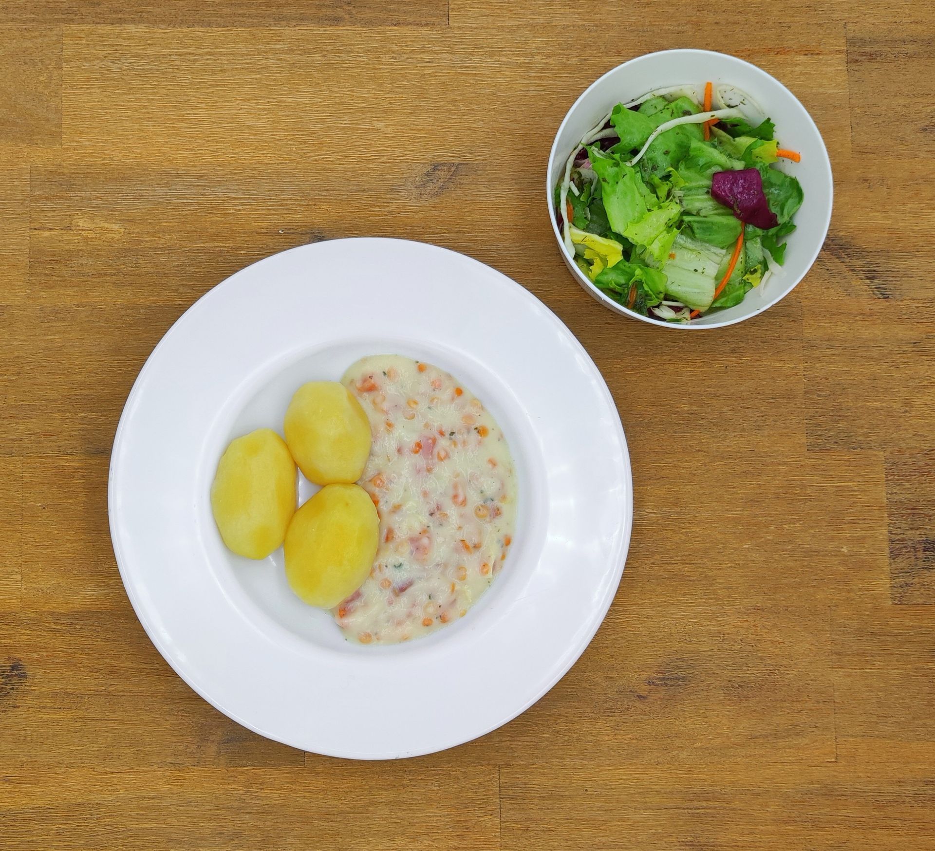 Auf einem weißen Teller mit Apfelmus lagen Crêpes auf einem Holztisch.