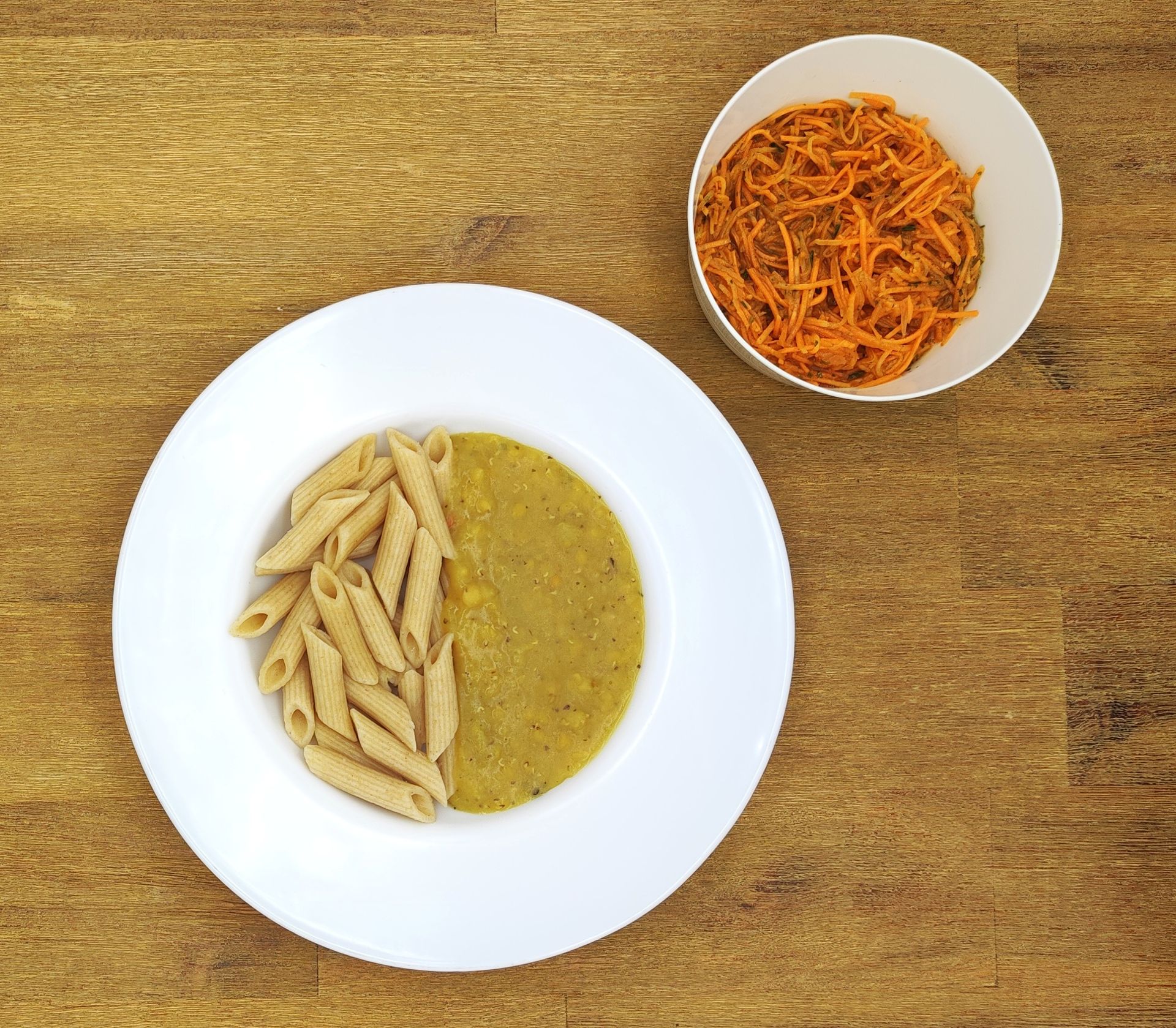 Weiße Schüssel mit Linsensuppe und Brot auf einer Holzoberfläche.