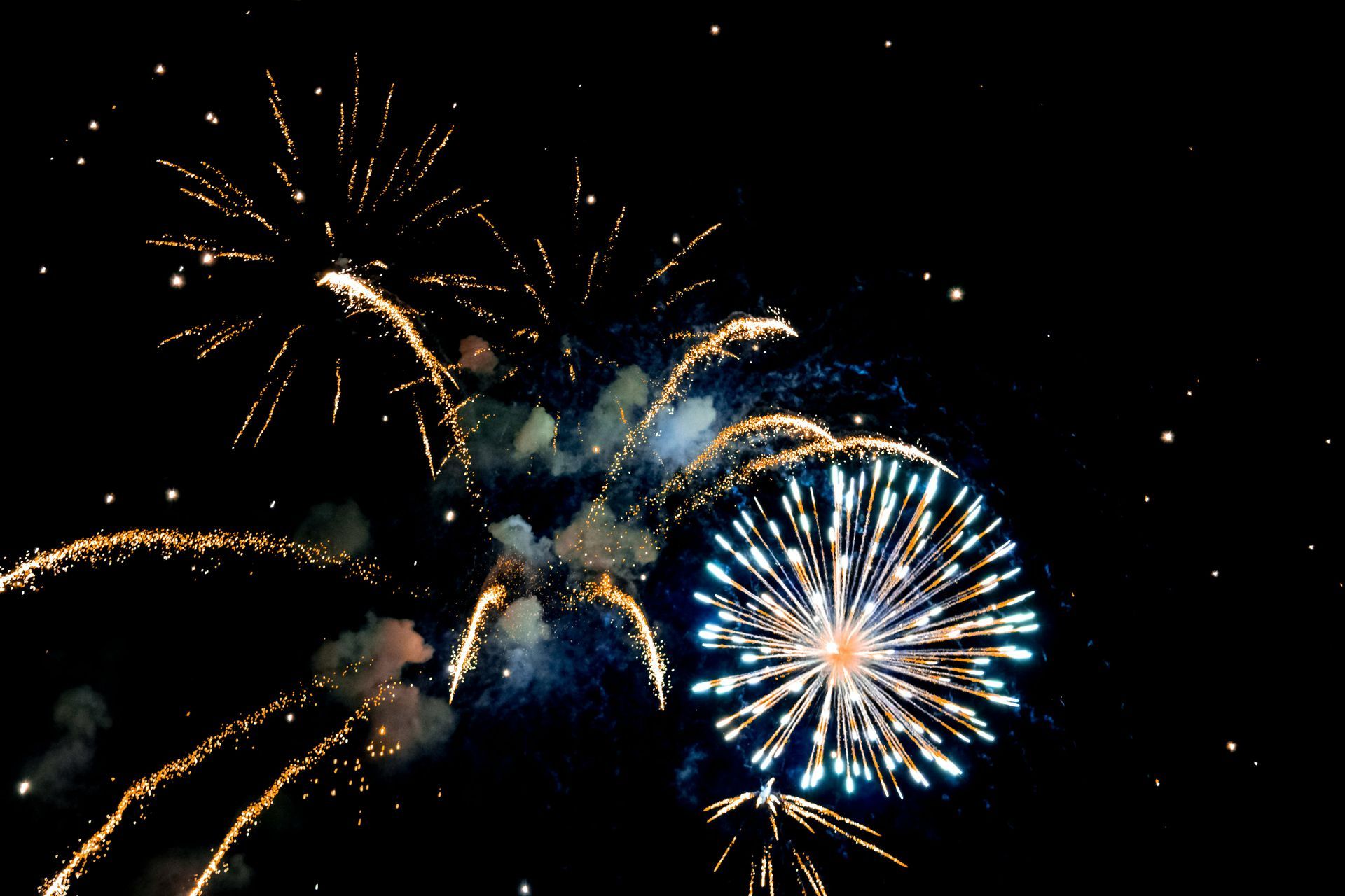 Feuerwerkskörper erhellen den dunklen Himmel; goldene und blaue Explosionen mit Lichtspuren.