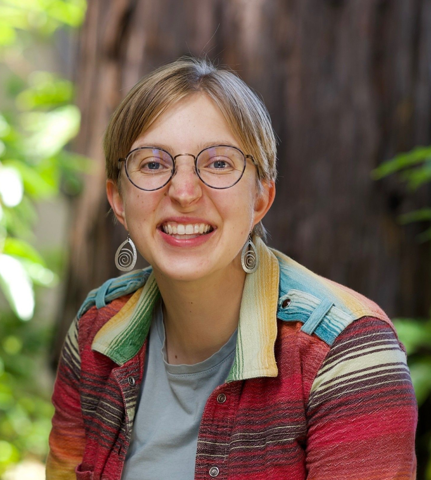 Smiling young woman with blonde hair and a red top, against a background of wildflowers.