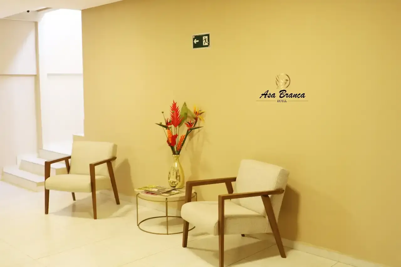 Uma sala de espera com duas cadeiras e uma mesa com um vaso de flores.hotel-asa-branca