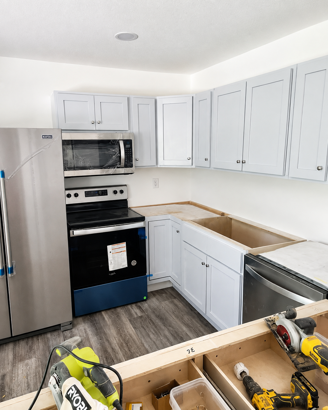 Kitchen under renovation with white cabinets, gray floor, and tools on a partially built island counter