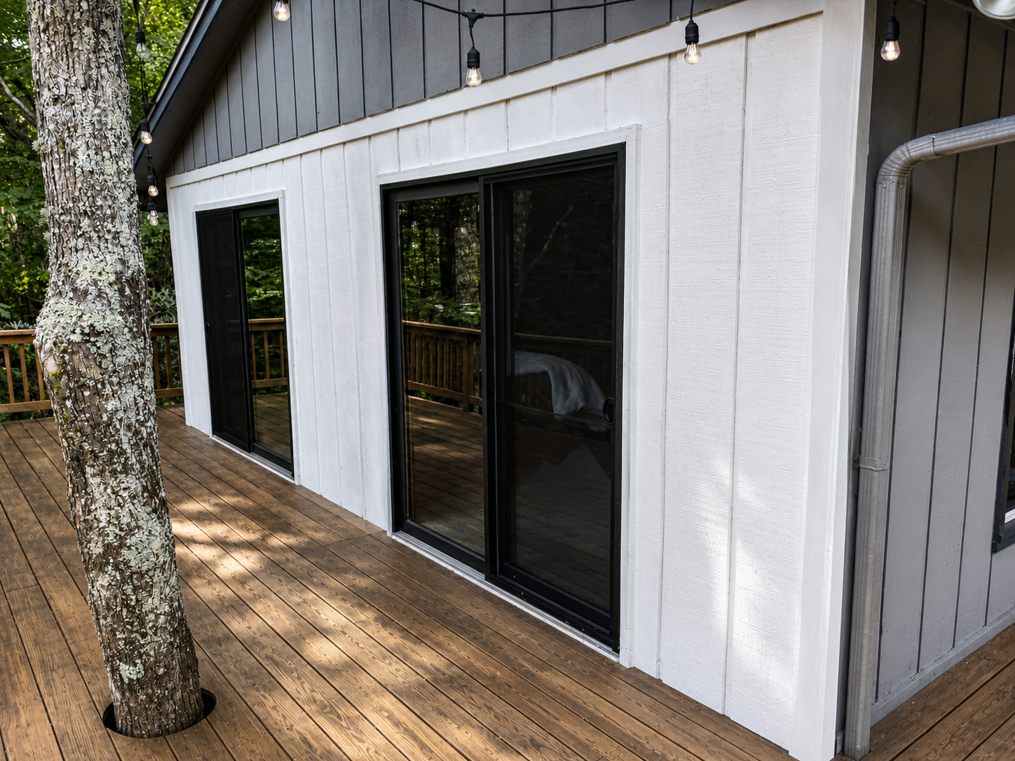 White house exterior with black sliding glass doors and a wood deck beside a tree