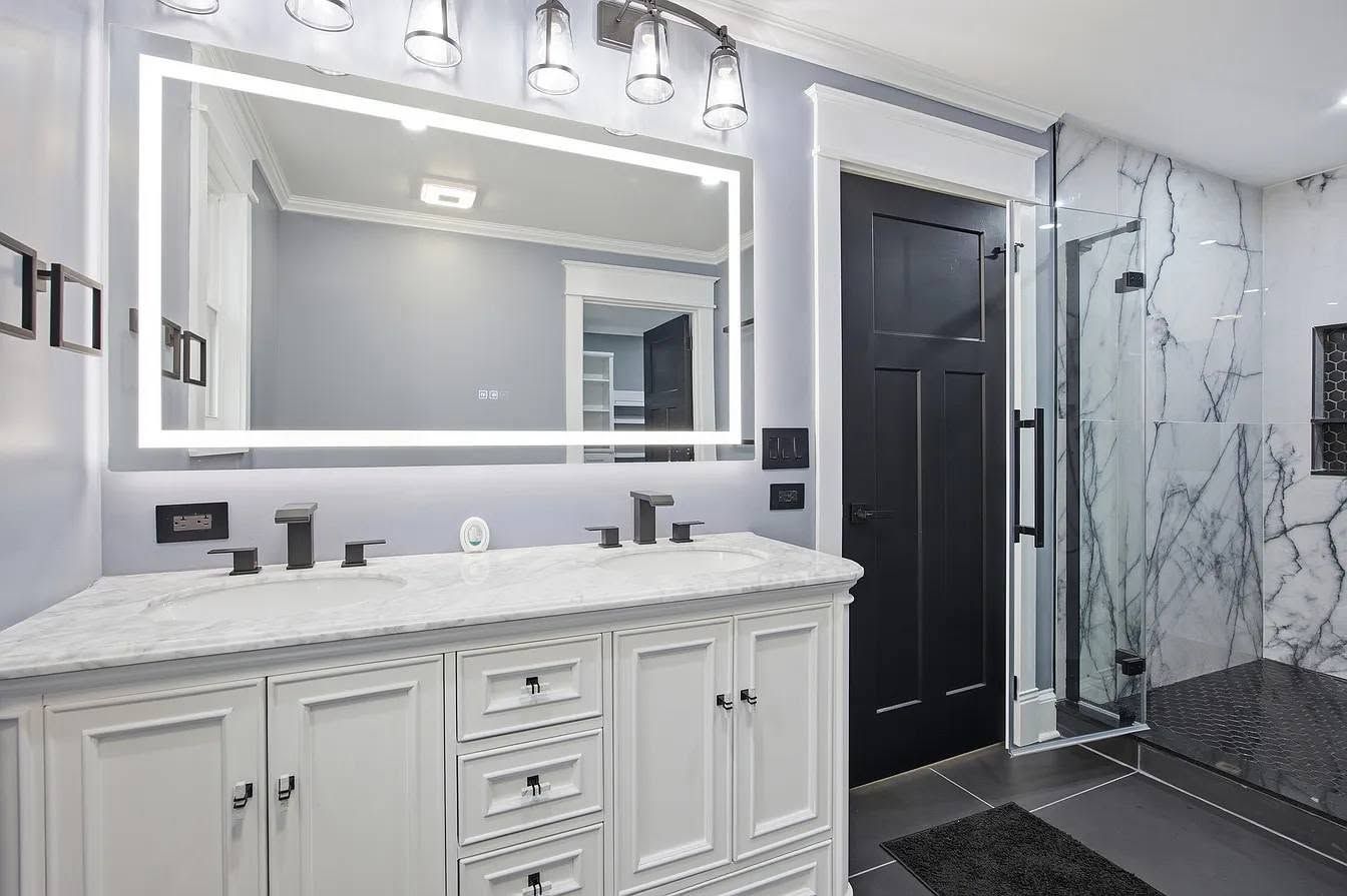 Modern white bathroom with double vanity, large mirror, black door, and marble shower walls