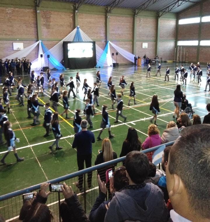 Evento en un gimnasio cubierto con mucha gente haciendo ejercicio en filas cerca de un escenario y una pantalla grande.