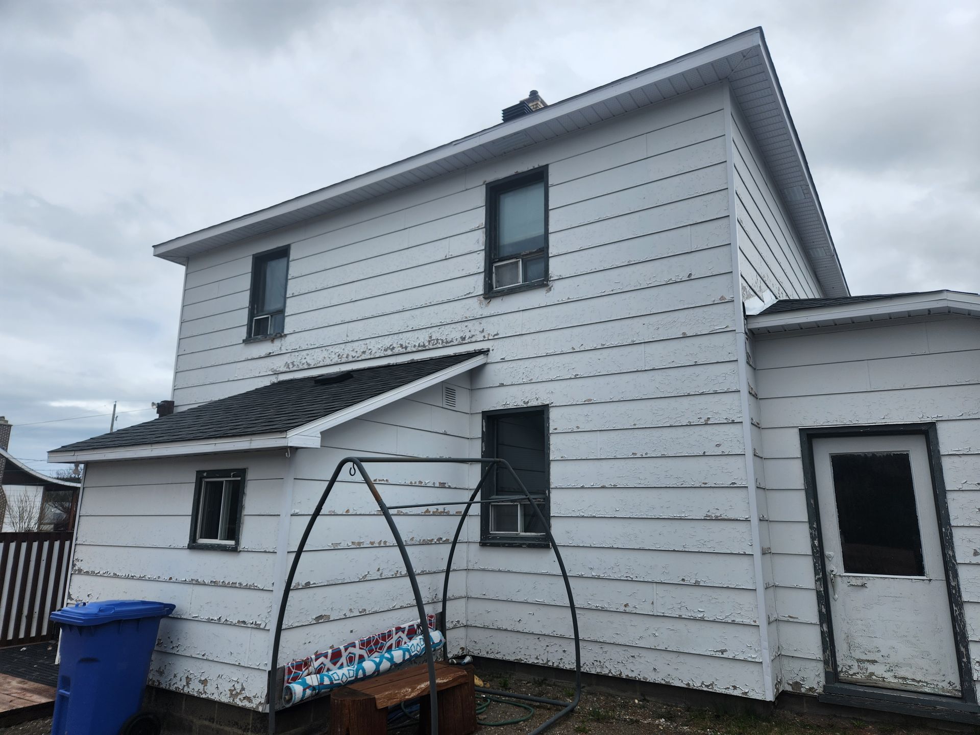 Une maison blanche avec une poubelle bleue devant.