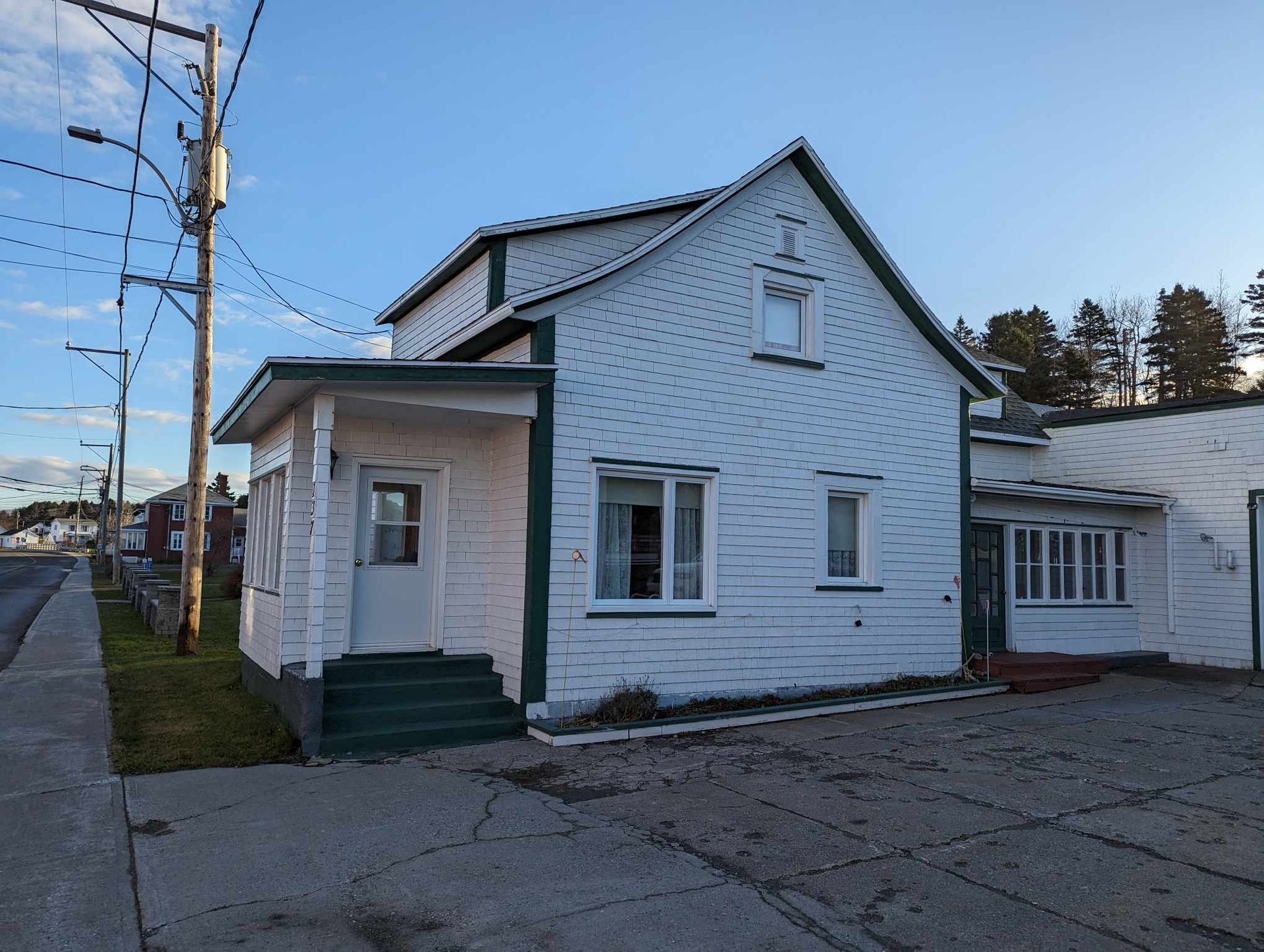 Une petite maison blanche avec des bordures vertes se trouve au coin d'une rue.