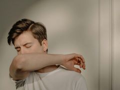A young man is coughing into his elbow.