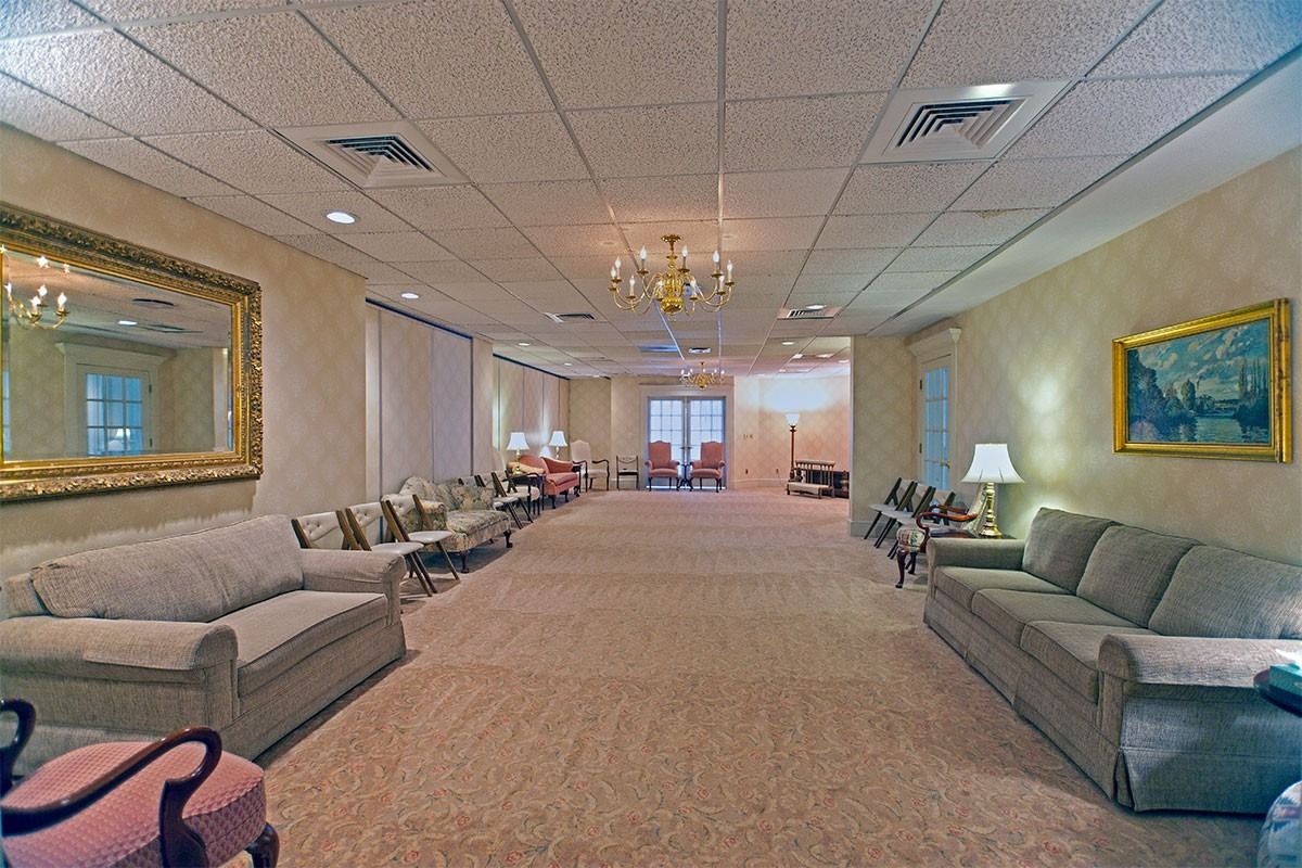 Wide, carpeted lobby with gray sofas, a chandelier, and double glass doors at the far end.