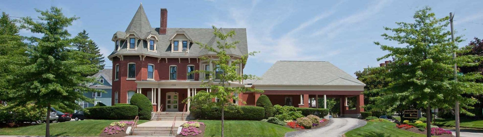Large brick house with a tower, green lawn, and trees on a sunny day