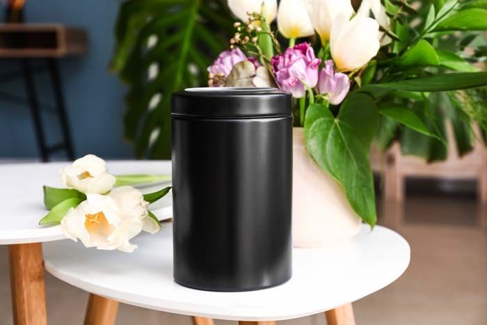 Black cylindrical candle tin on a white table with white and pink flowers in the background