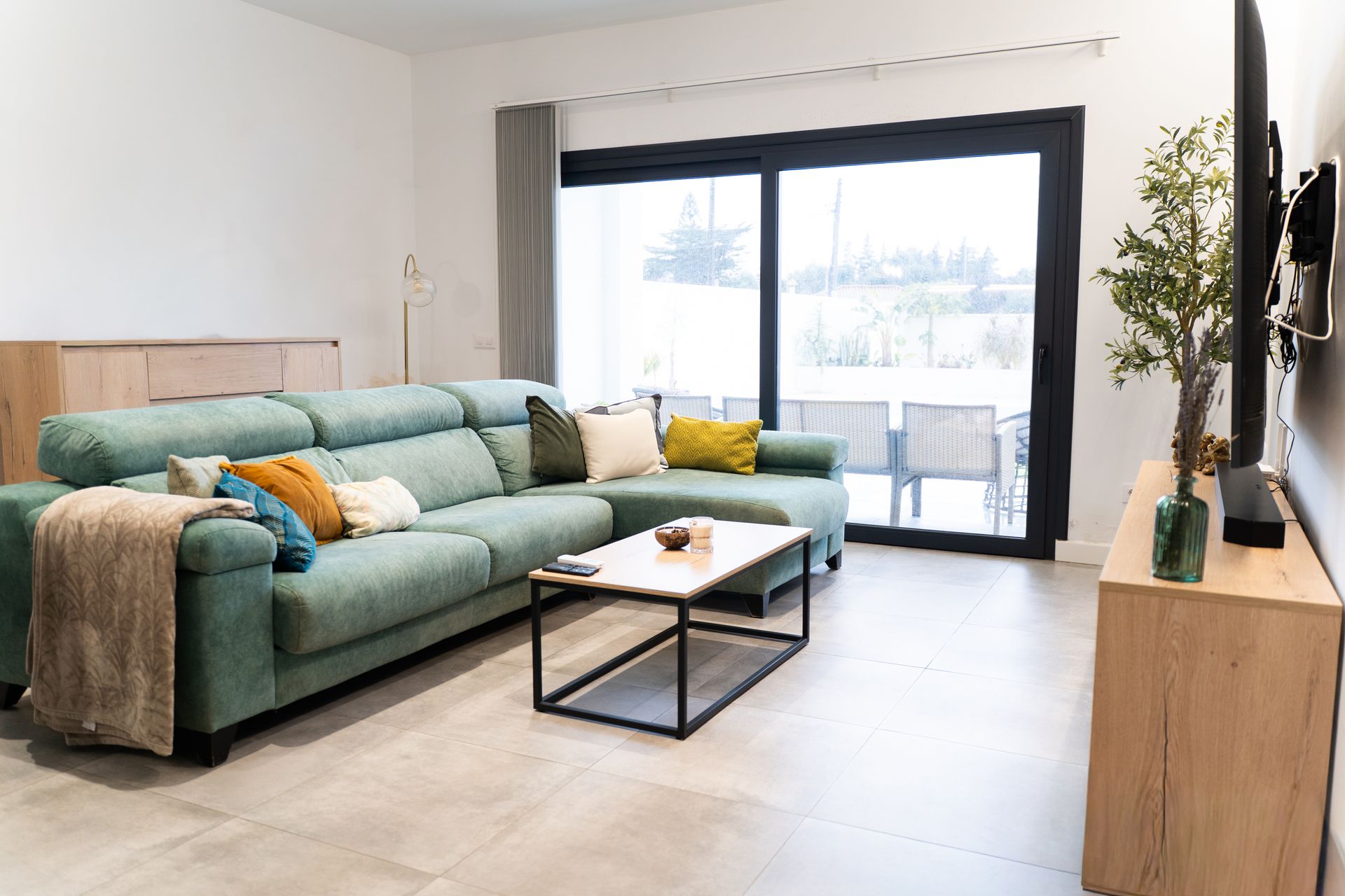 Modern living room with a teal sofa, large sliding glass doors, and a bright outdoor view.